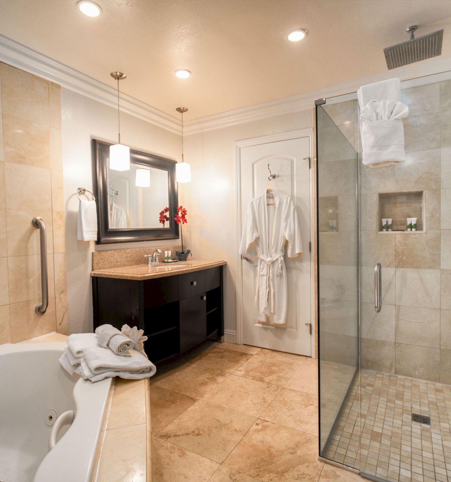 This image shows a luxurious bathroom with a bathtub, glass-enclosed shower, vanity with mirror, hanging robes, and a towel rack with folded towels.