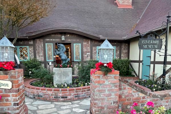 A quaint building with a pitched roof, brick path, statue, and garden. Sign reads “ELVERHØJ MUSEUM.”.