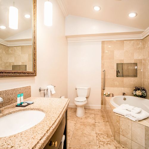 This image shows a modern bathroom with a granite countertop, large mirror, toilet, bathtub, glass shower enclosure, and tiled walls and floor.