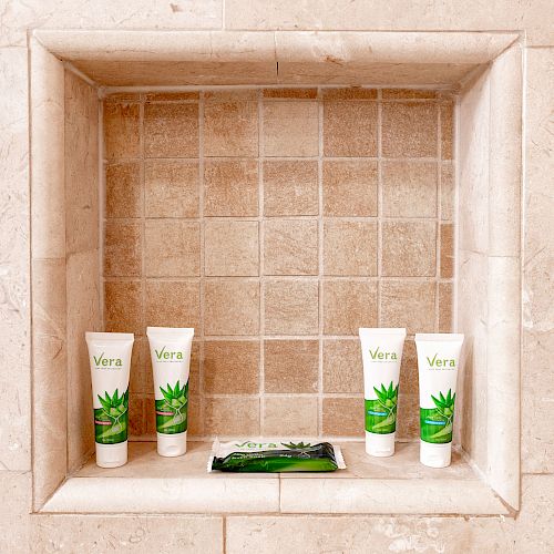 A tiled shower niche holding five skincare products, including tubes and a small packet, all labeled with 