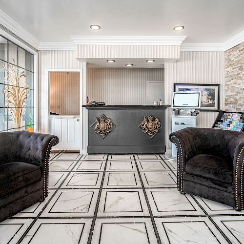 A modern reception area features two black armchairs, a counter with decorative accents, a computer, a brochure stand, and large windows.