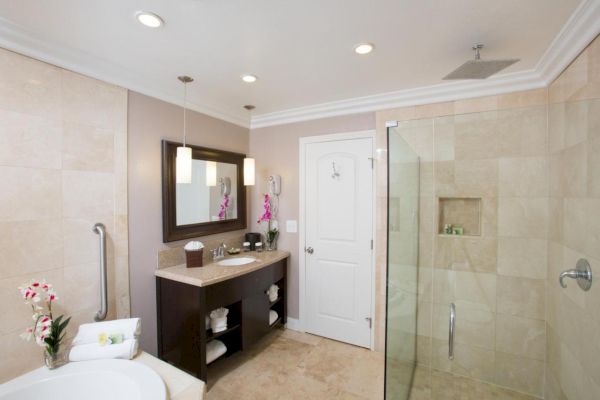 A modern bathroom with a glass shower, bathtub, vanity with double sinks, mirror, and decorative plants, all in a beige and white color scheme.