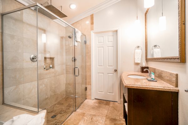 This image shows a modern bathroom with a glass-enclosed shower, a vanity with a sink and mirror, and minimalistic decor in neutral tones.