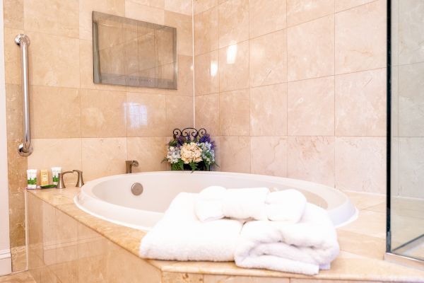 A luxurious bathroom with a marble bathtub, fluffy towels, toiletries, and a bouquet of flowers. The space is well-lit and elegant.